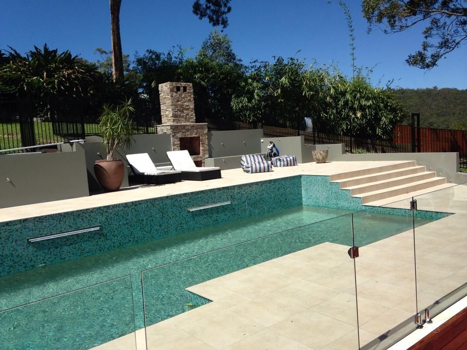 Modern backyard pool with glass fence, lounge chairs, and a built-in grill area