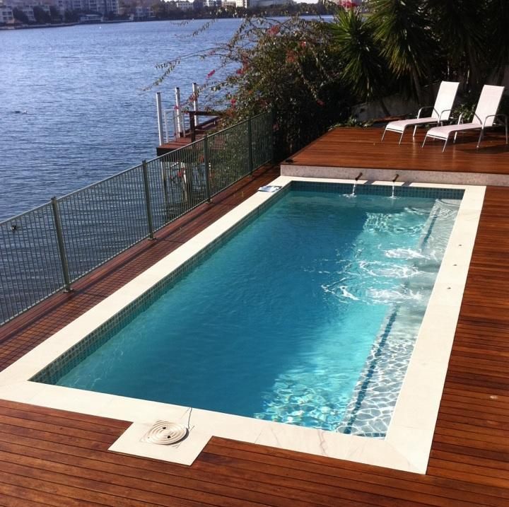 Small deck with rectangular pool overlooking water, with white lounge chairs and city skyline in the distance