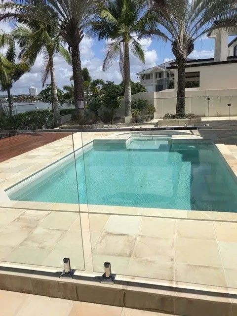 Glass-fenced pool with turquoise water, palm trees, and a waterfront view