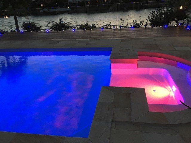 Blue-lit pool beside a pink-lit hot tub at night on a patio