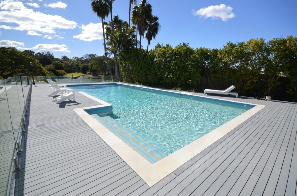 Modern outdoor swimming pool with lounge chairs and a gray deck under a sunny sky