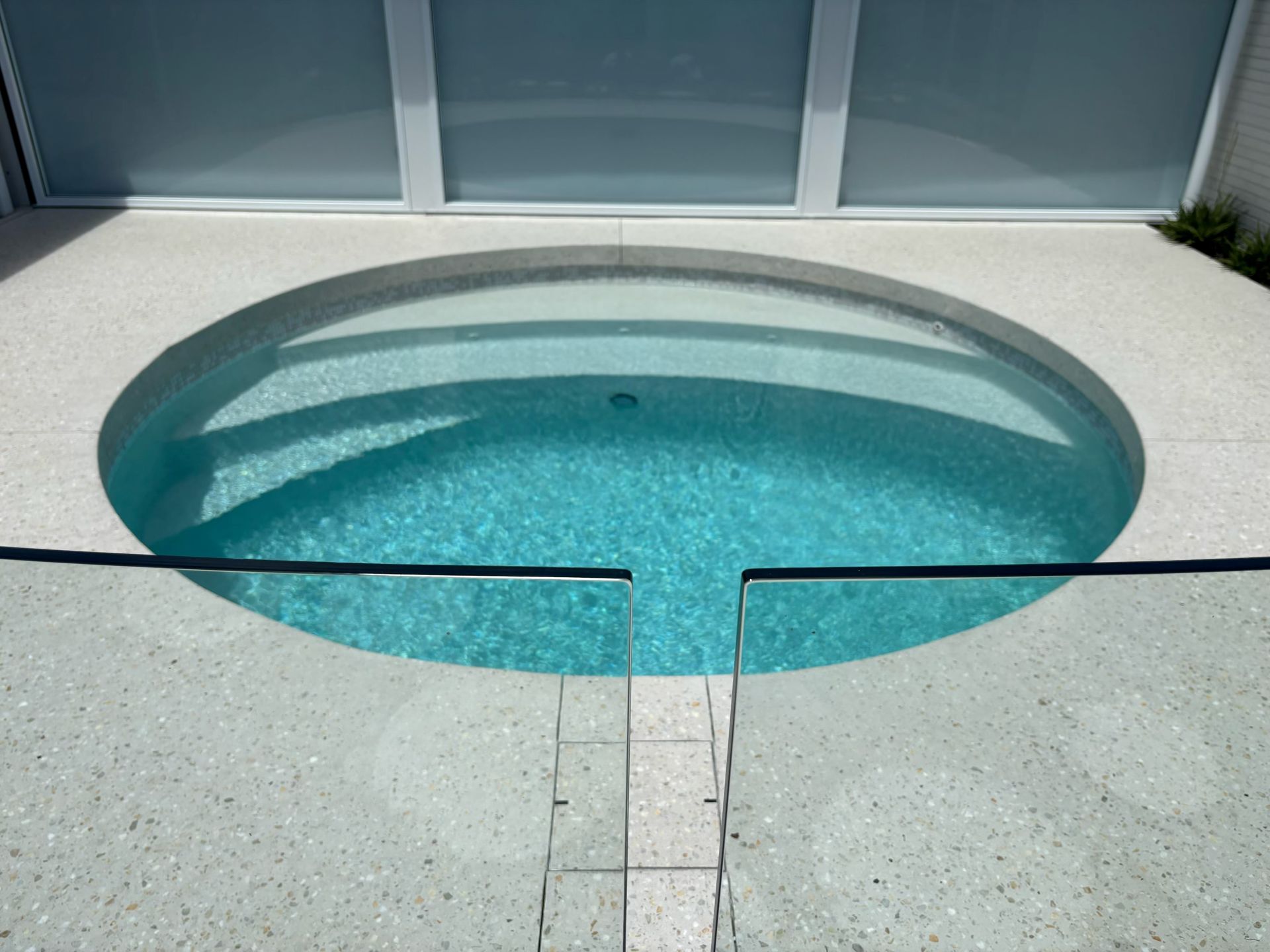 Oval swimming pool with turquoise water beside a light gray deck and glass railing