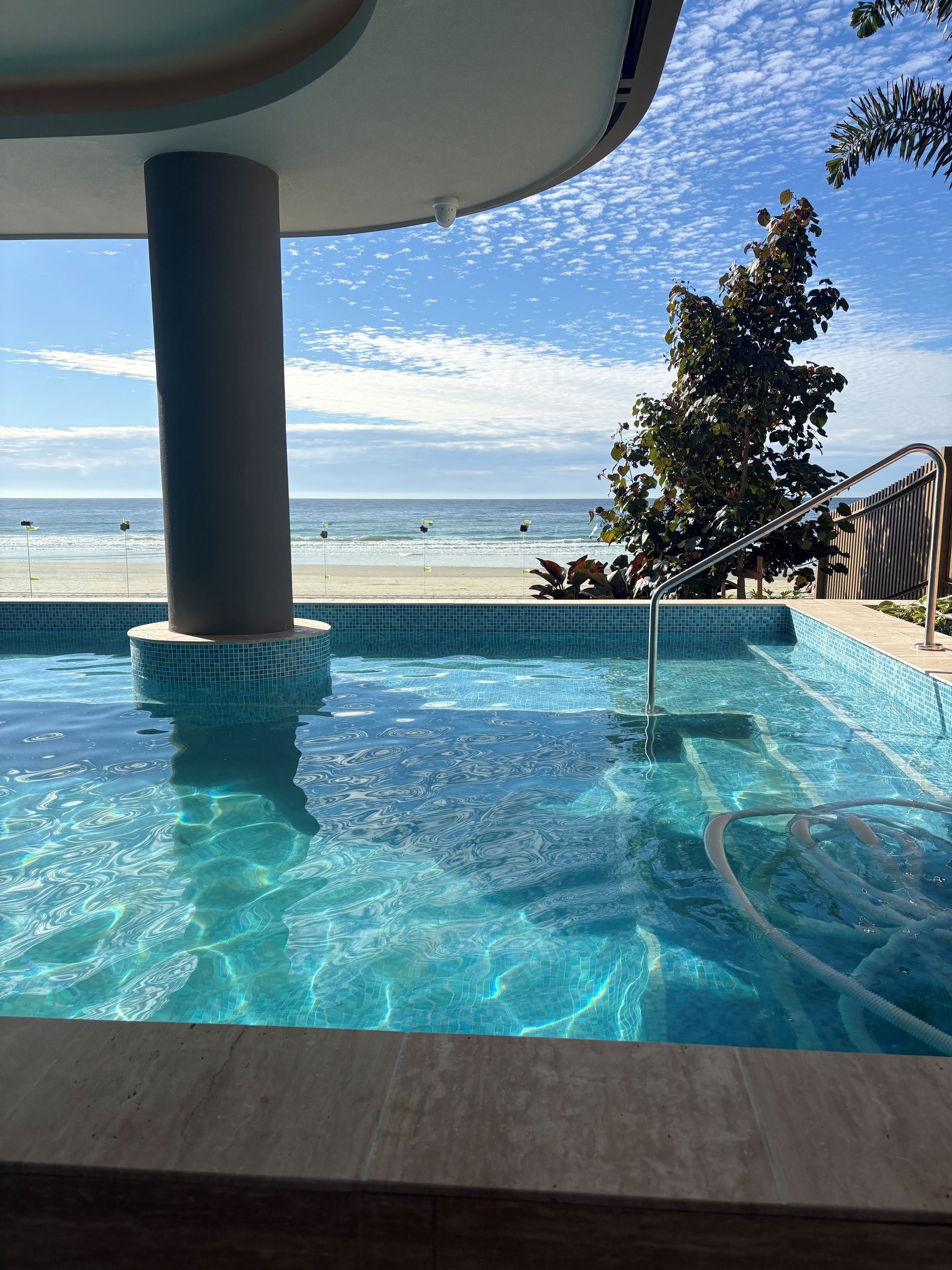 Ocean-view infinity pool with turquoise water, modern canopy, and beach umbrellas under a blue sky