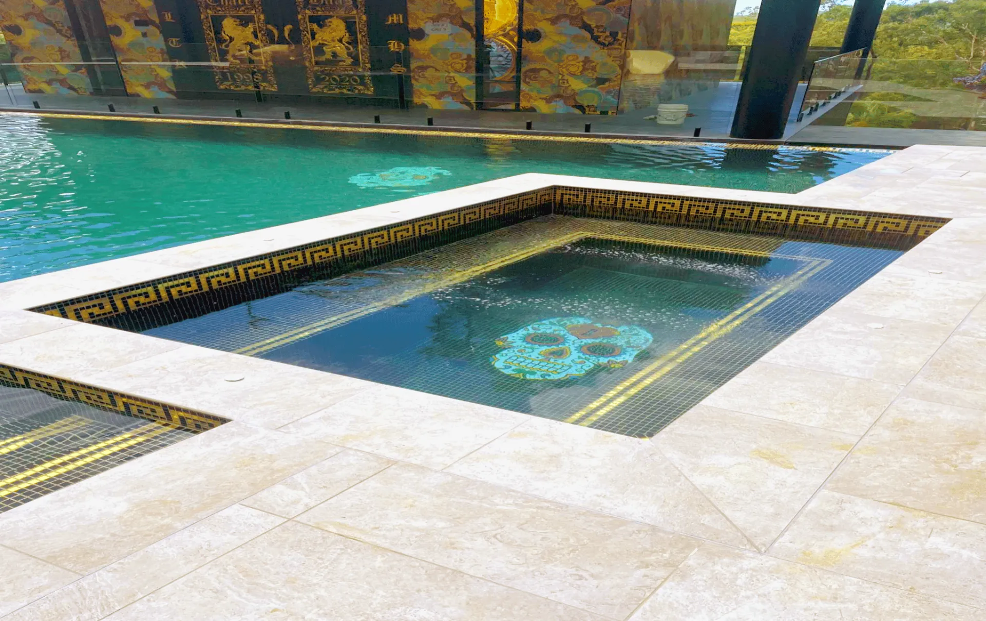 Outdoor pool with a square hot tub, turquoise water, and autumn trees in the background