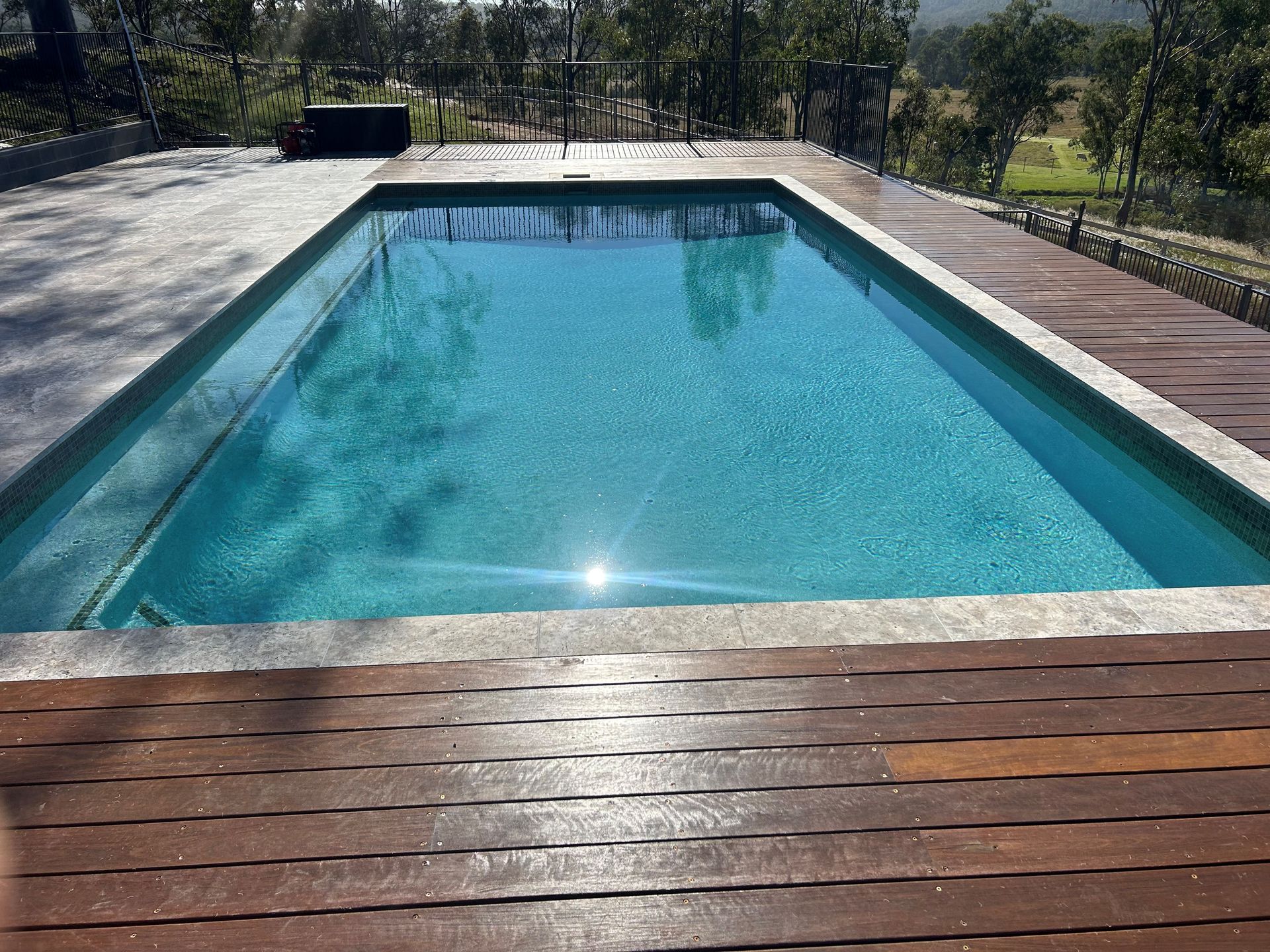 Rectangular backyard swimming pool with clear blue water and a wooden deck in the foreground