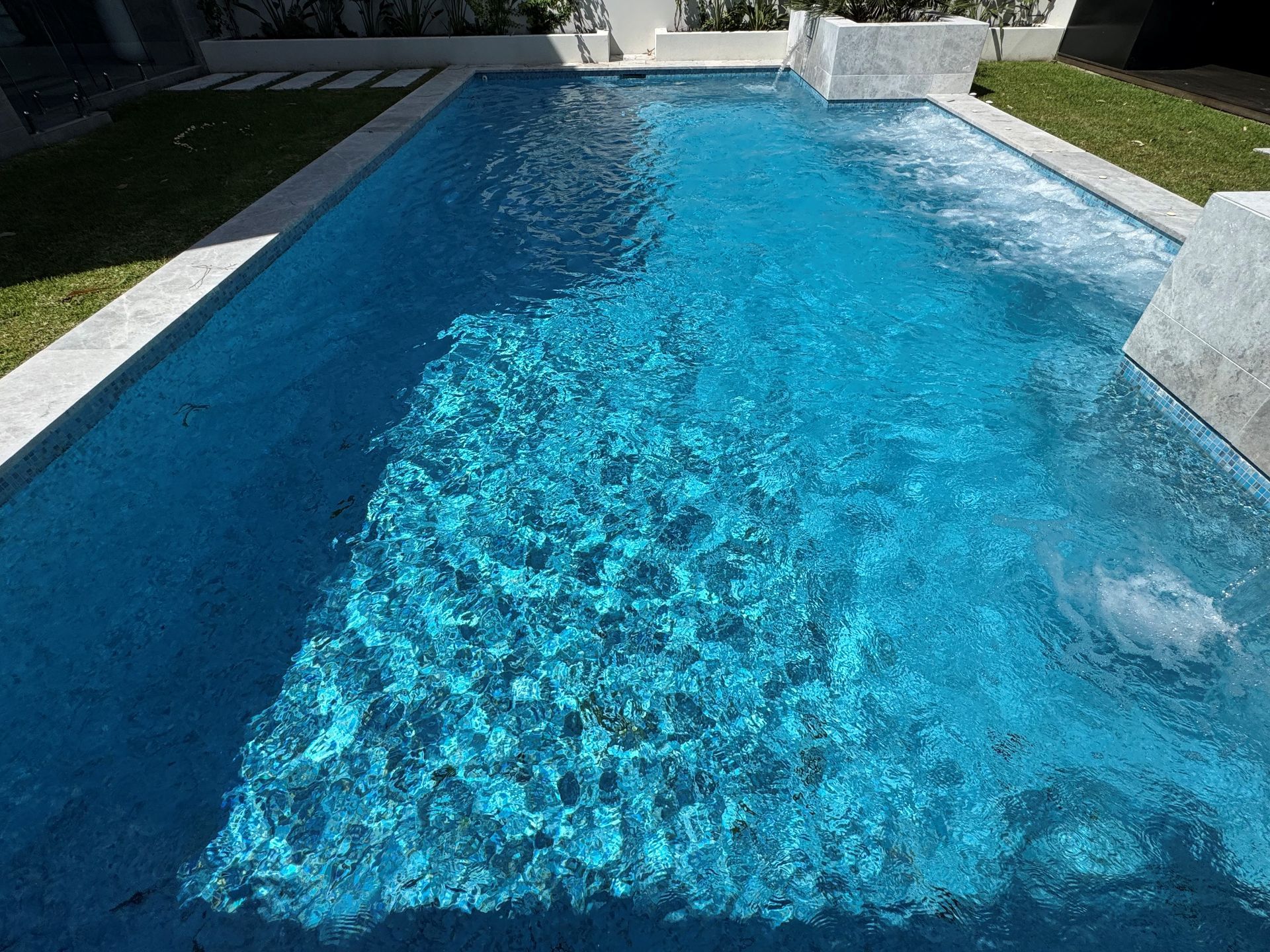 Blue swimming pool with clear water and white stone edges in a sunny backyard
