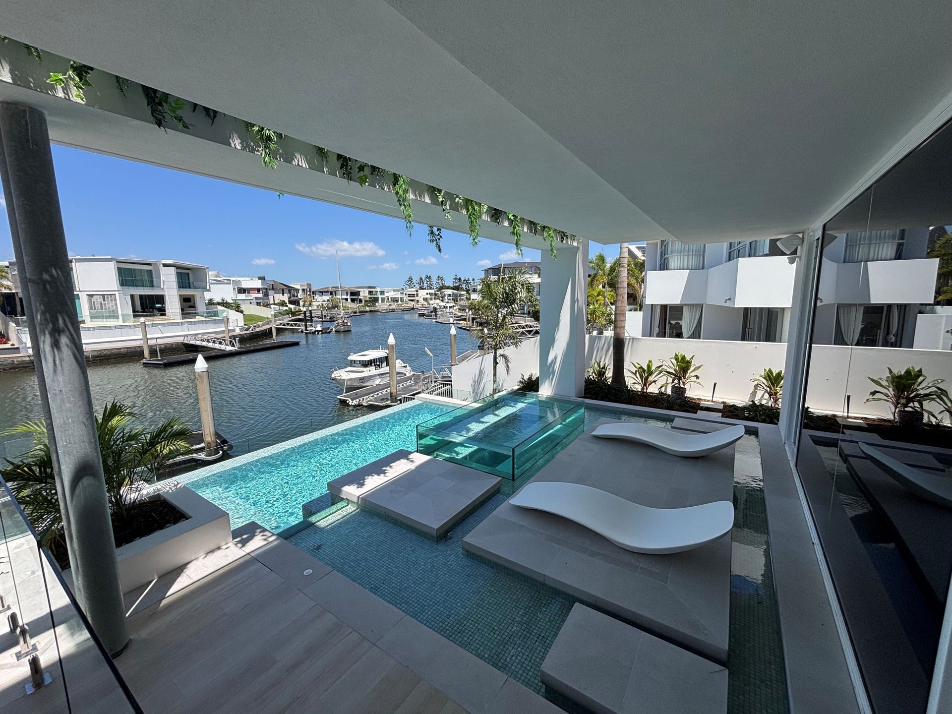 Modern waterfront patio with pool, lounge chairs, and canal view under a shaded pergola
