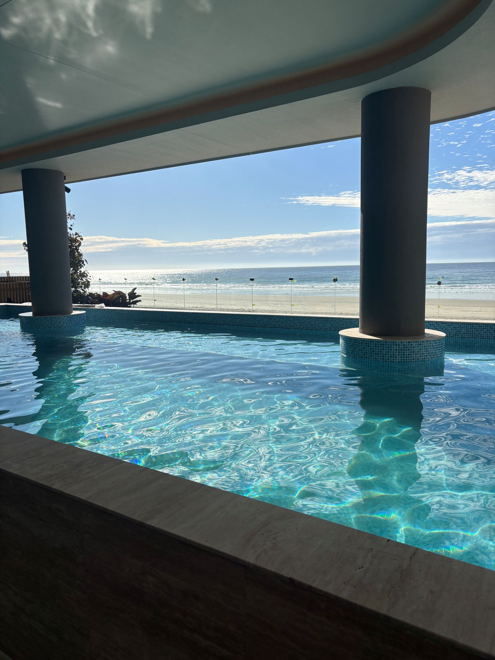 Infinity pool under a shaded terrace overlooking a calm blue ocean and cloudy sky