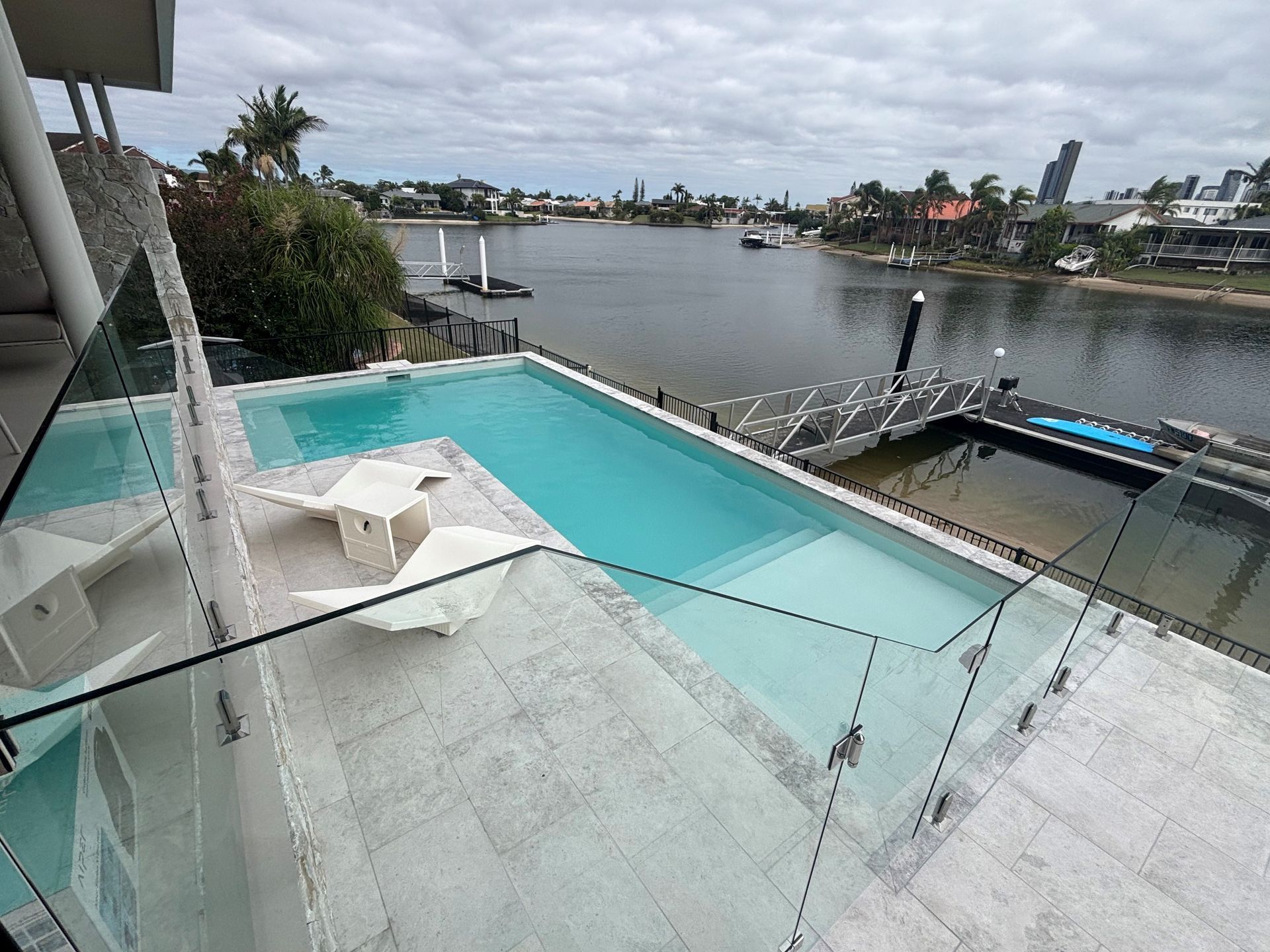 Rooftop infinity pool overlooking a canal, with lounge chairs and waterfront homes beyond.