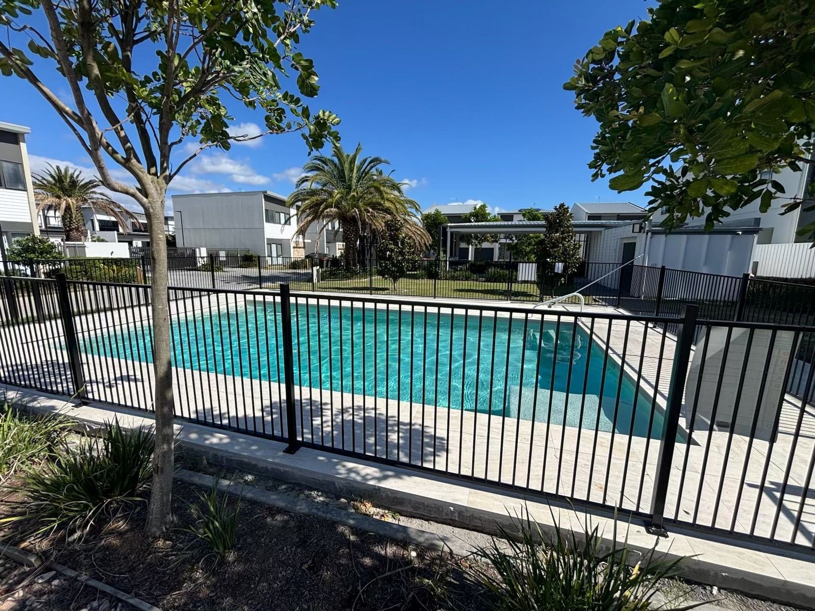 Apartment pool behind black metal fence under a clear blue sky