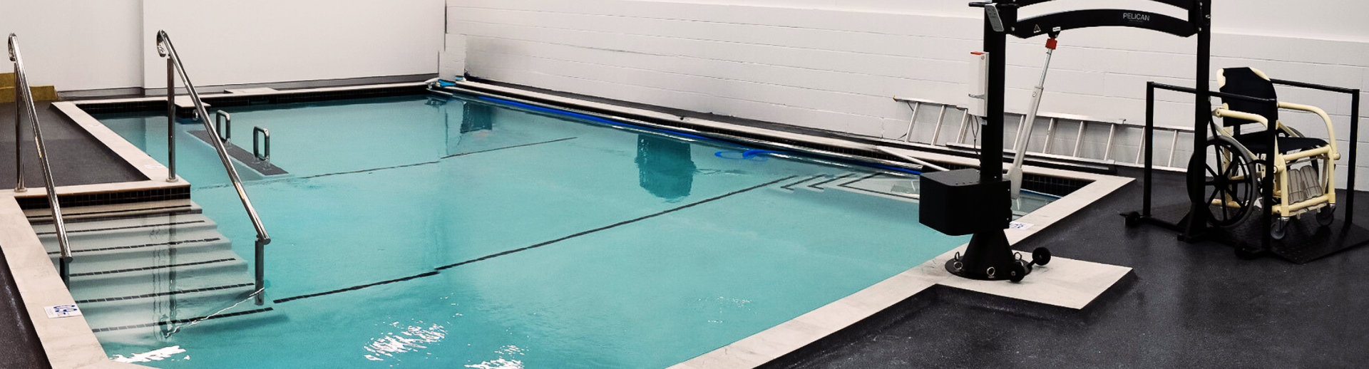 Small indoor swimming pool with turquoise water, metal handrails, and lounge chairs beside a tiled deck.