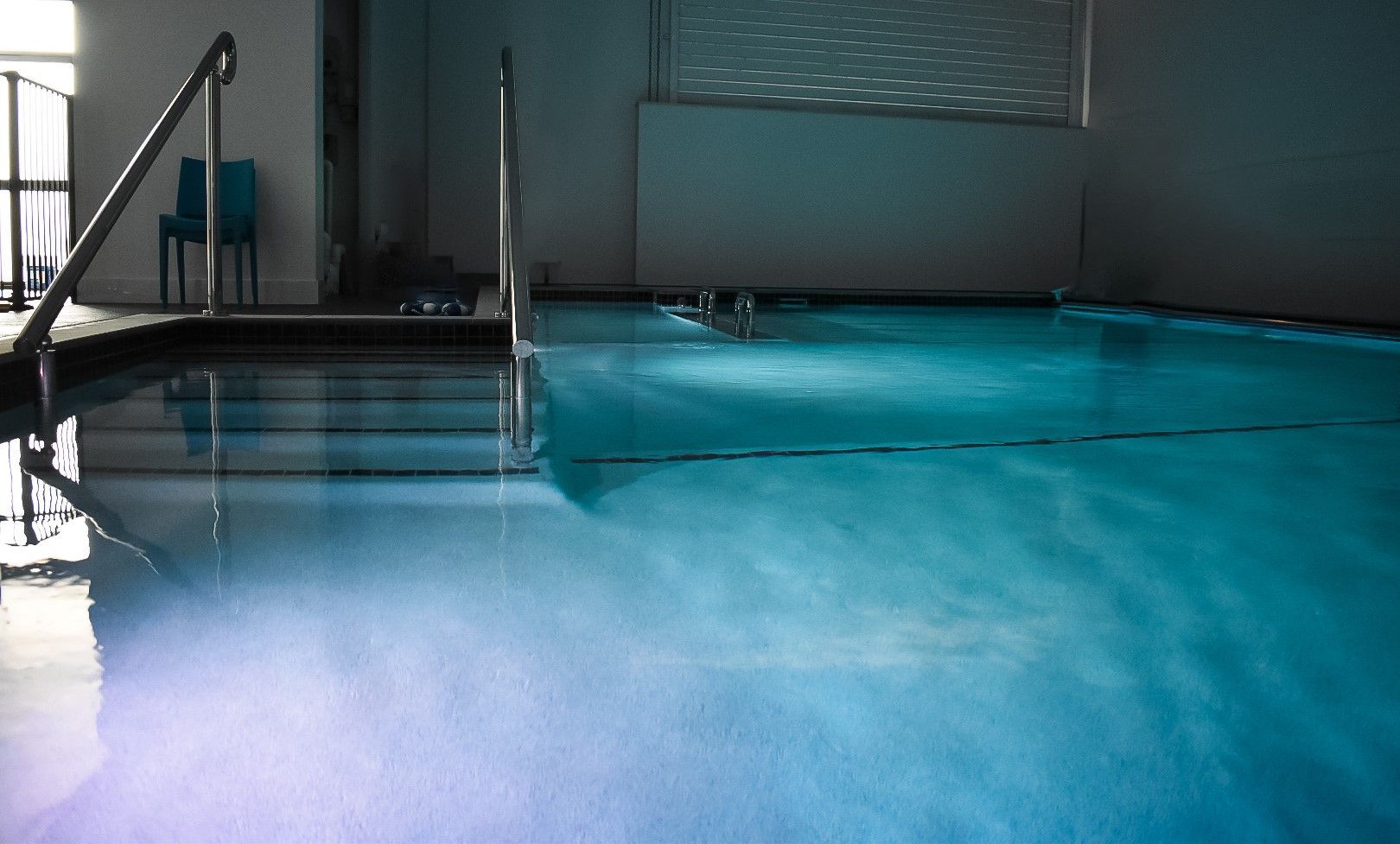 Indoor swimming pool with turquoise water, lane markings, and pool deck reflections