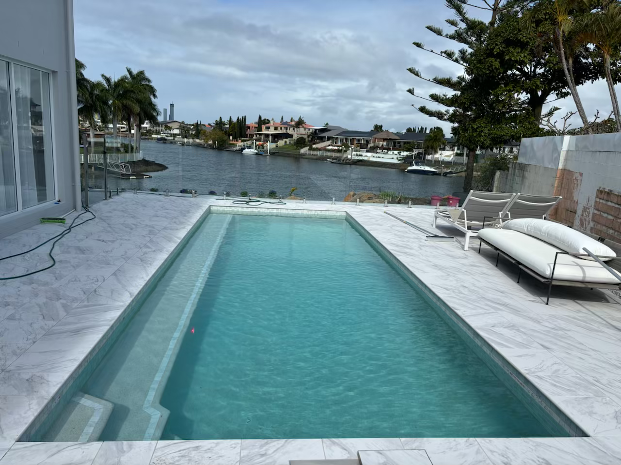 Modern backyard pool beside a waterfront, with lounge chairs and a cloudy sky