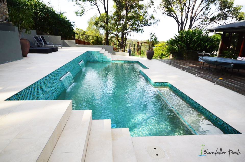 Modern backyard pool with turquoise water, white deck, and steps surrounded by tropical greenery