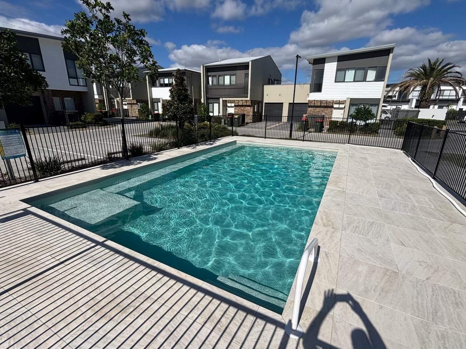 Modern house backyard with a rectangular swimming pool and white deck under a blue sky