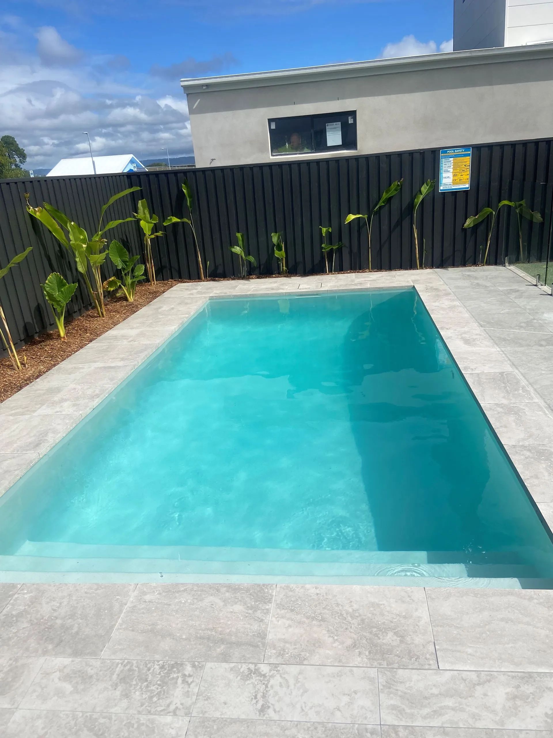 Small backyard swimming pool with turquoise water, gray pavers, black fence, and a house in the background
