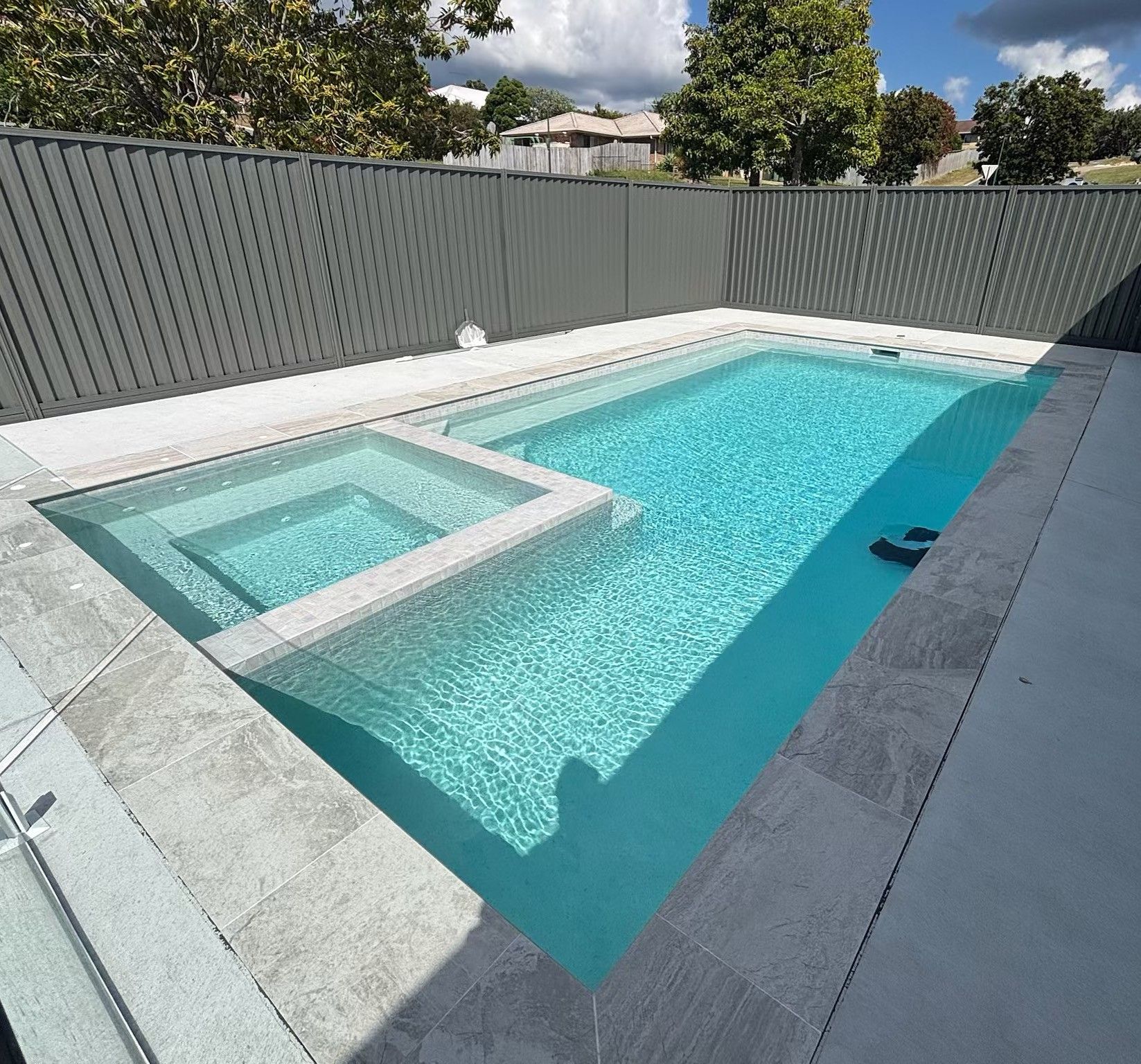 Rectangular backyard swimming pool with a raised square spa and light stone decking under sunny skies