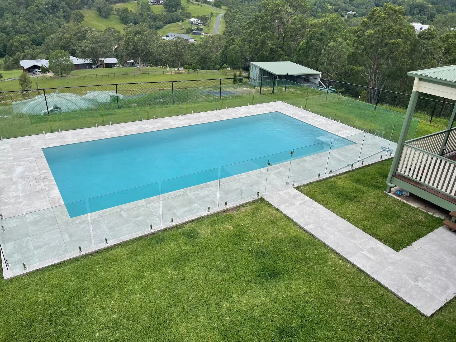 Outdoor swimming pool with blue water, surrounded by a white deck and green lawn in a hillside setting