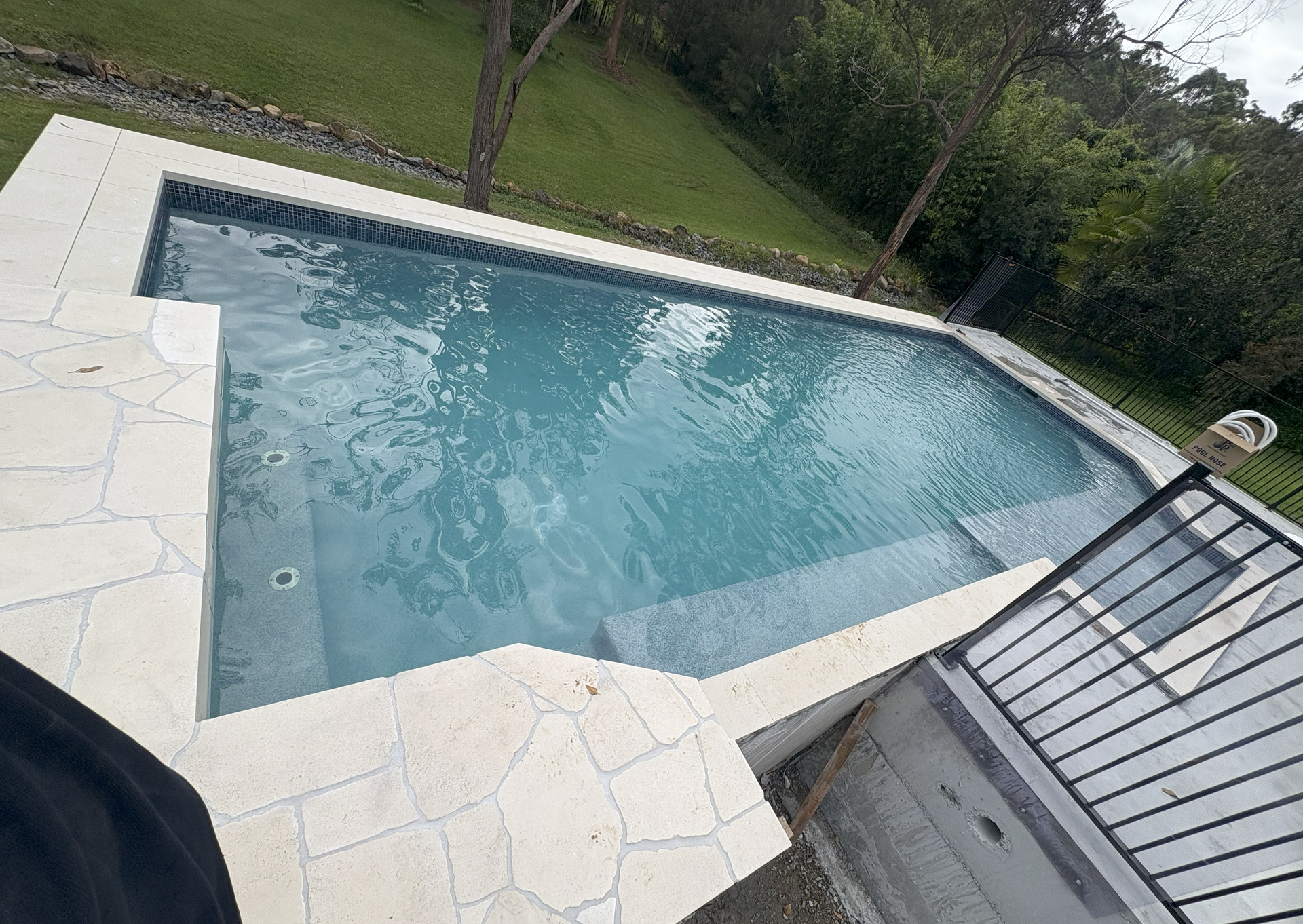 Empty outdoor swimming pool with light blue water and white tile decking beside a grassy yard.