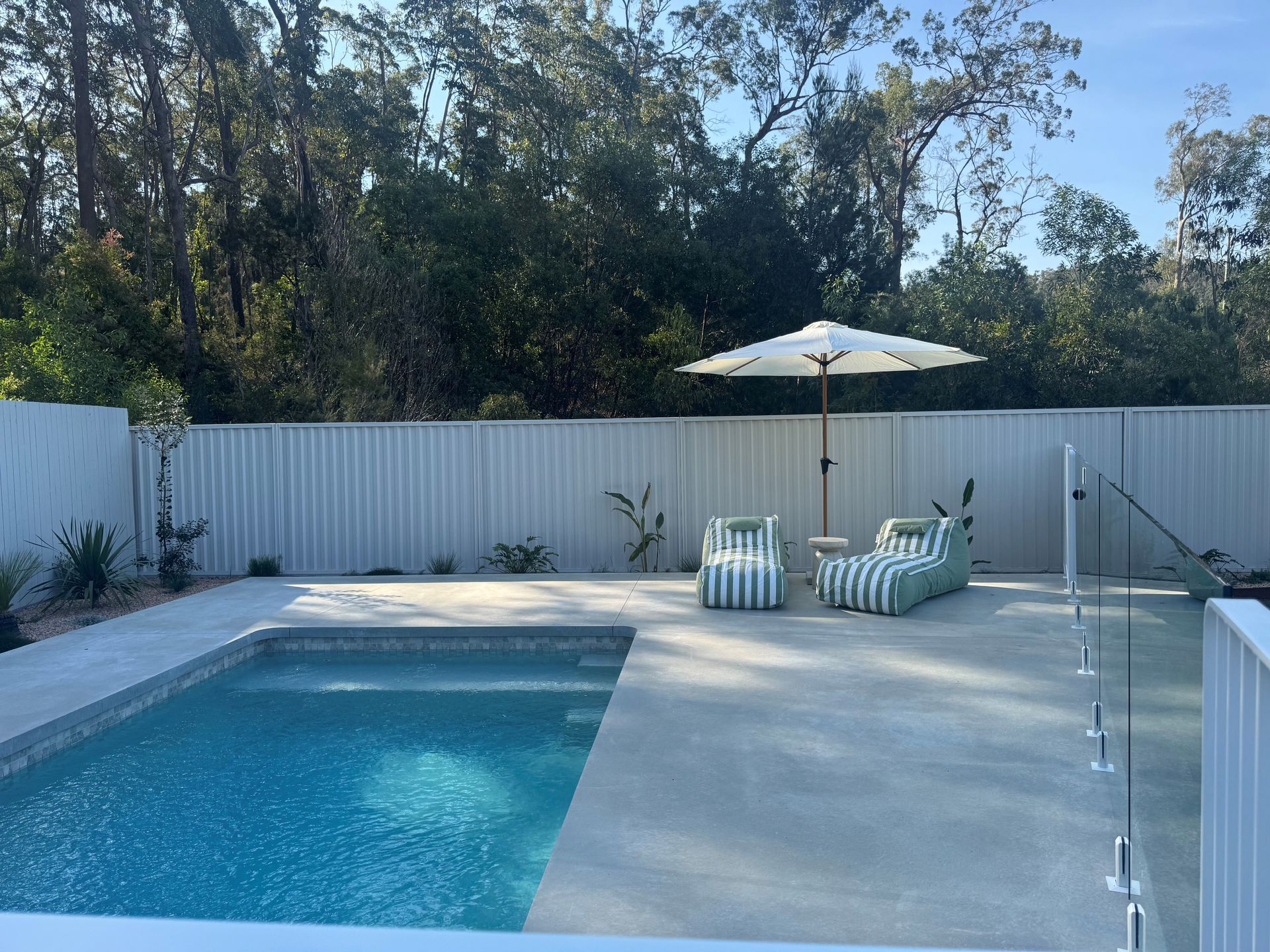 Backyard swimming pool with lounge chairs, umbrella, and white privacy fence
