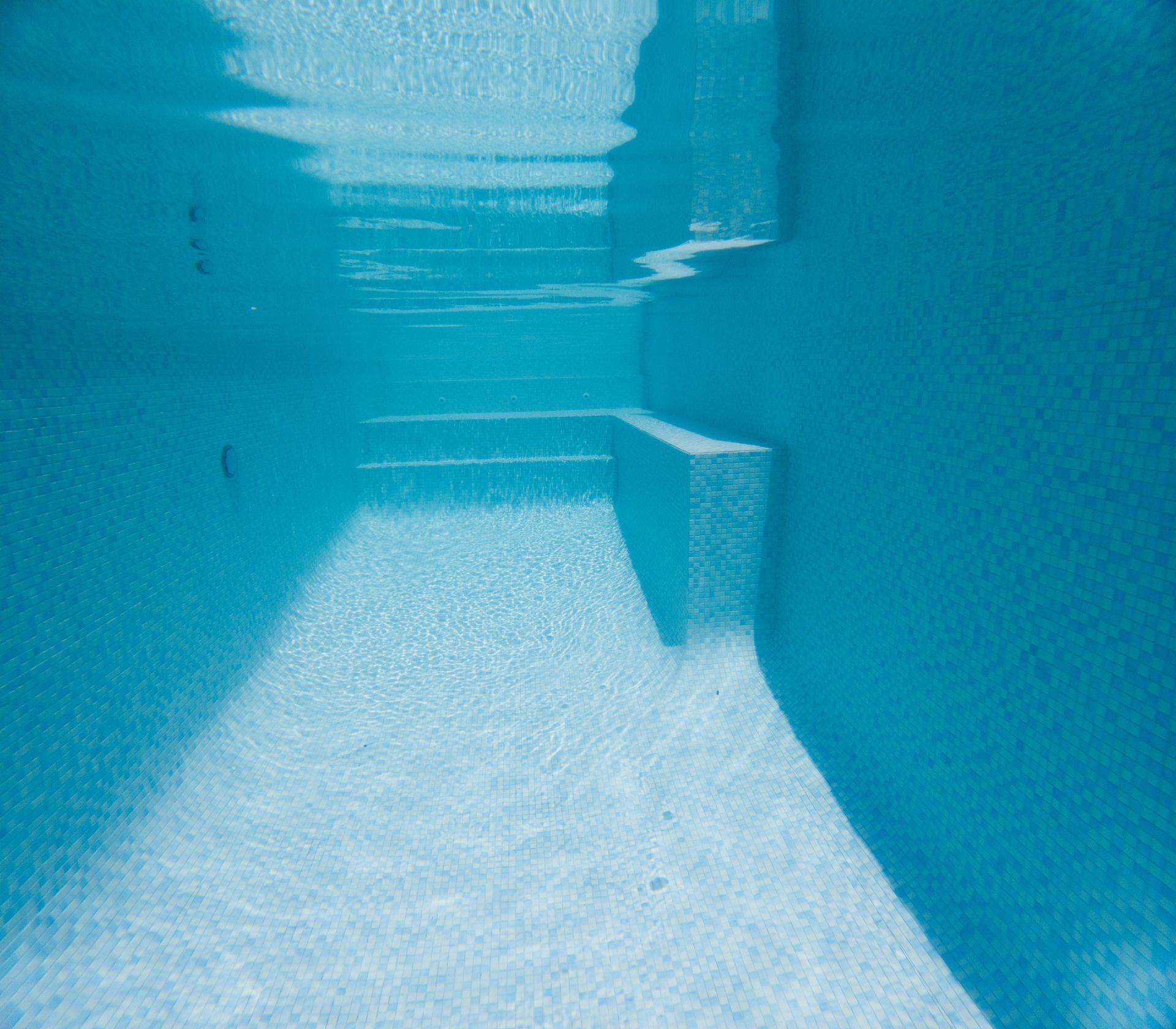 Empty turquoise swimming pool with clear water and bright sunlight reflections