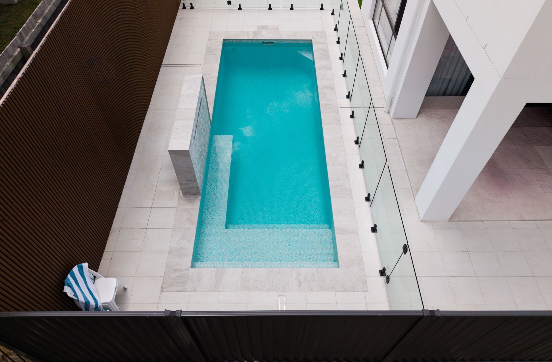 Rooftop pool with turquoise water beside a white building and glass railing