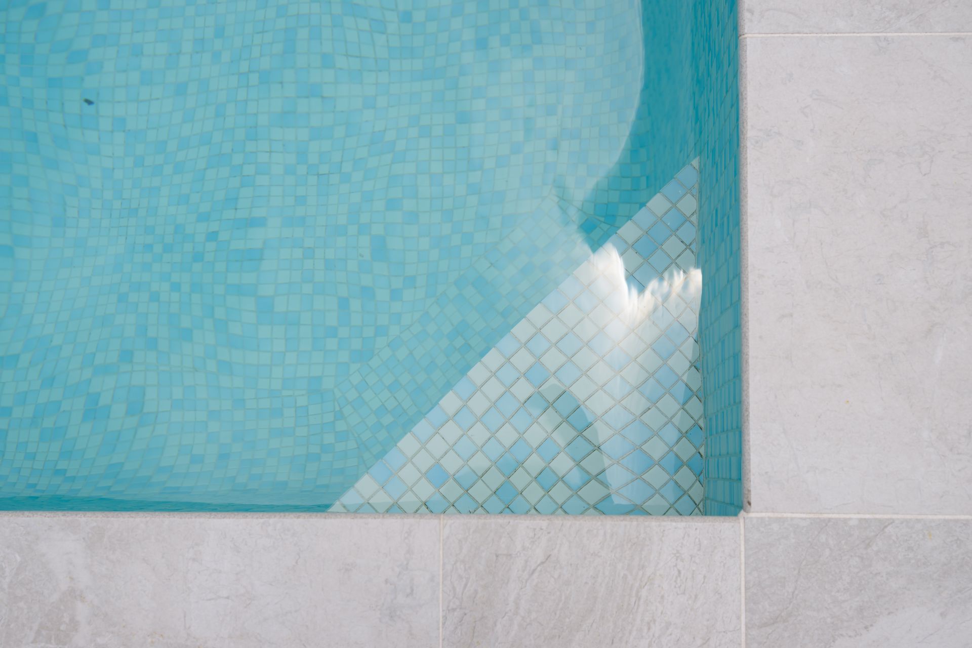 Blue swimming pool corner with tiled edge and light gray deck tiles