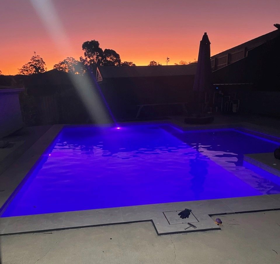 Backyard pool glowing blue at sunset under a pink-orange sky