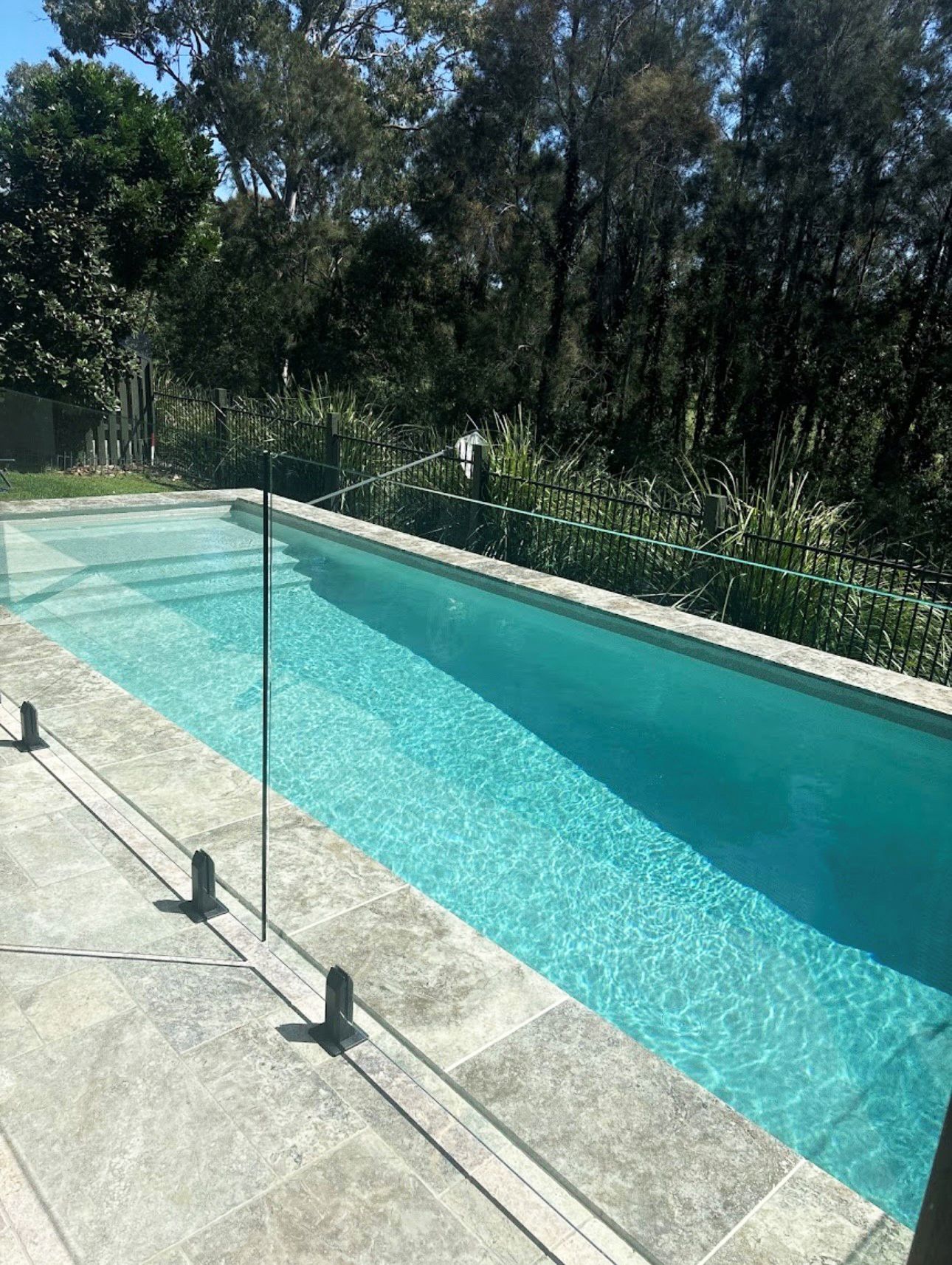 Outdoor swimming pool with turquoise water, glass railing, and trees in the background