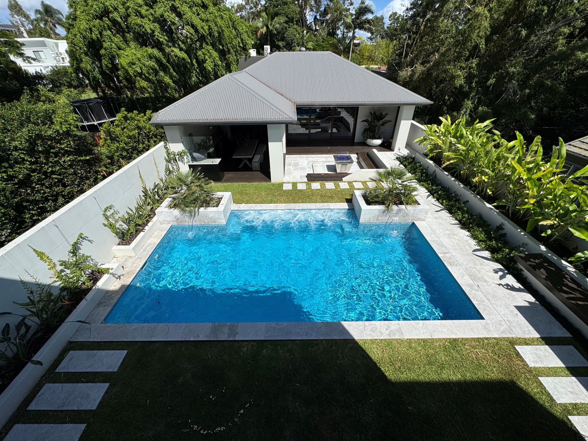 Modern backyard with a rectangular blue pool, white walls, and a shaded patio pavilion