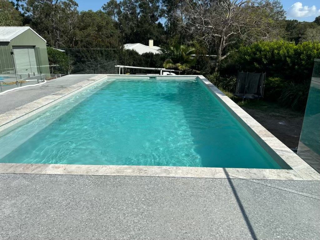 Rectangular turquoise swimming pool beside a concrete deck and trees on a sunny day