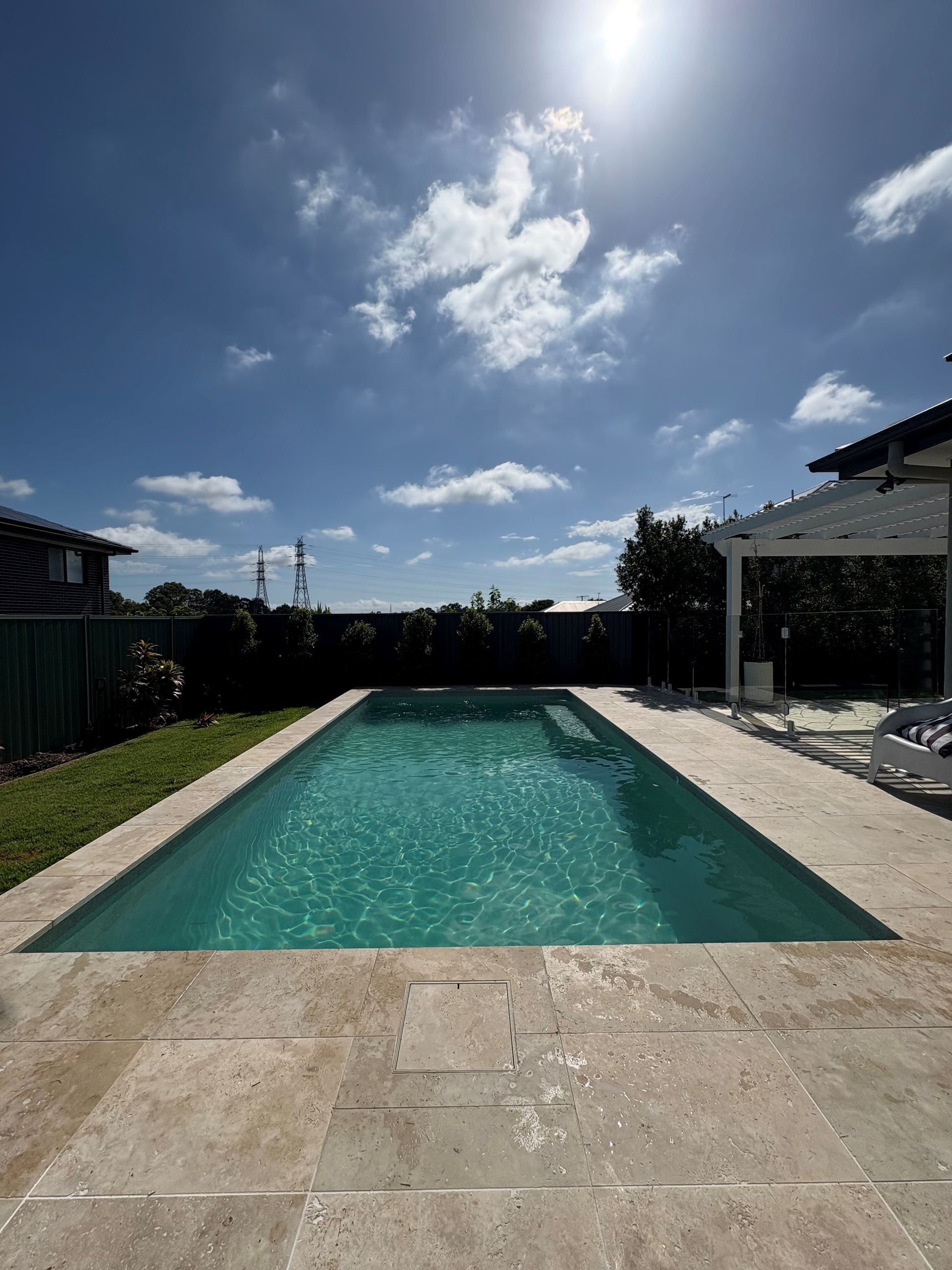 Backyard swimming pool under bright sunny sky, with stone deck and pergola