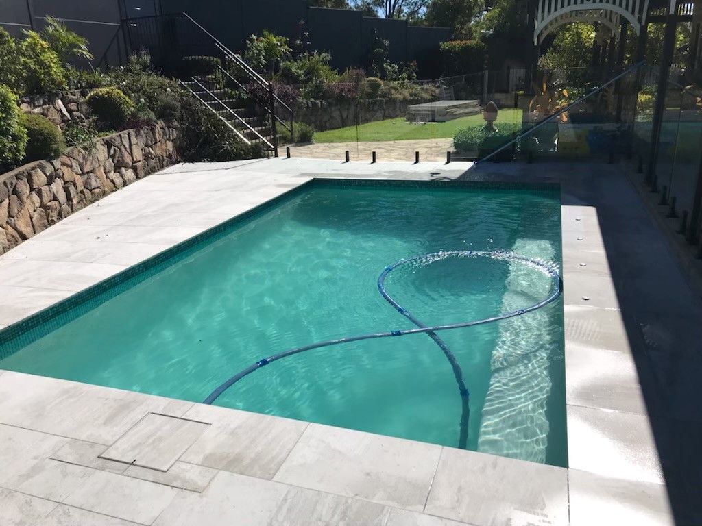 Backyard swimming pool with turquoise water, white deck, stone wall, and garden stairs in the background