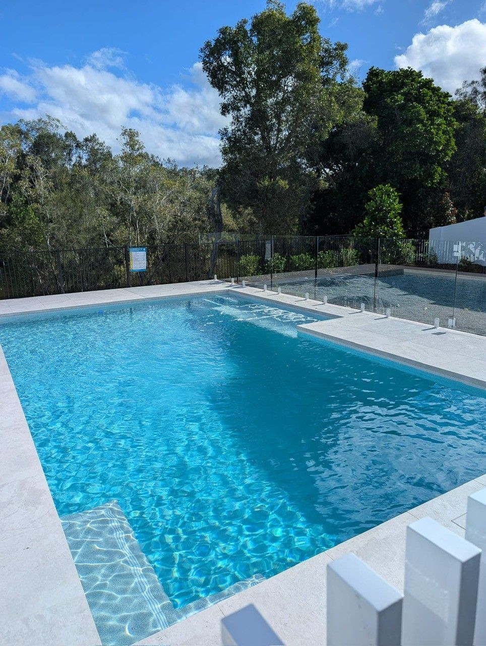 Outdoor swimming pool with clear blue water, white deck, and trees in the background