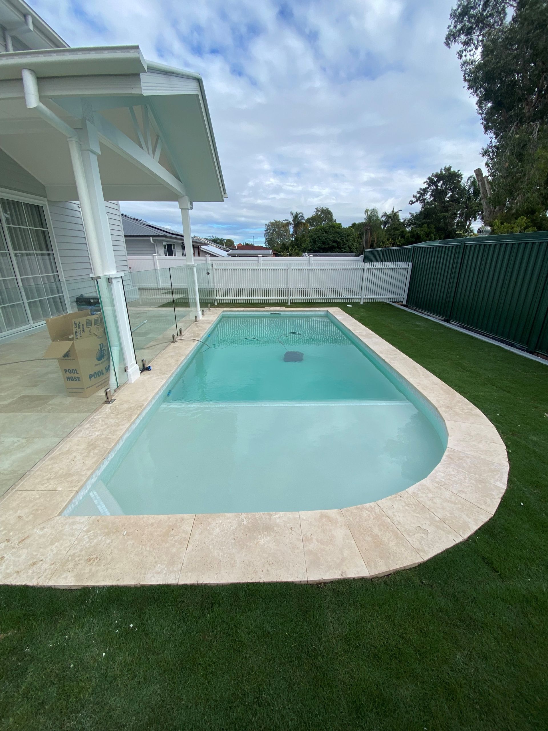 Backyard swimming pool with a curved shallow edge, white patio, and green lawn beside a house