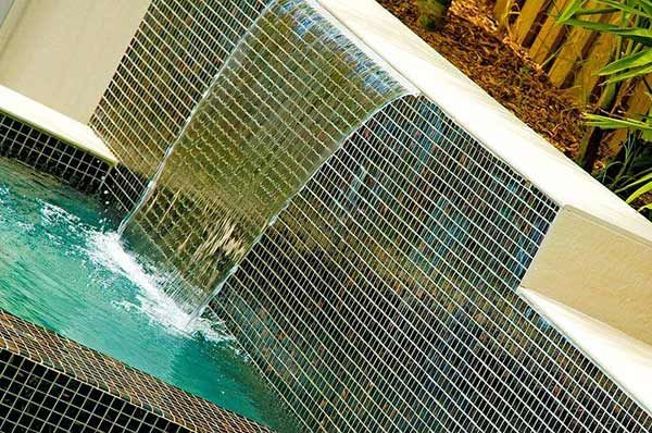Diagonal view of a small waterfall spilling into a turquoise pool beside a tiled wall