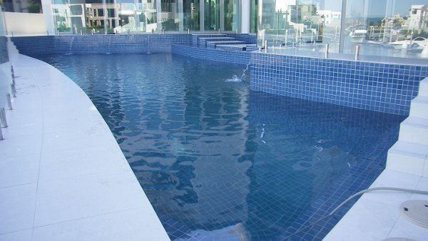 Modern outdoor swimming pool with blue tiled water and white deck, overlooking nearby buildings