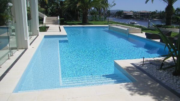 Modern outdoor swimming pool with blue water beside a white patio and palm trees