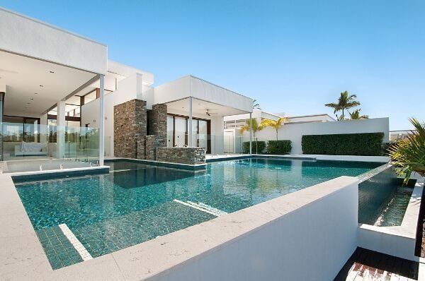 Modern white villa with a turquoise infinity pool and palm trees under a clear sky