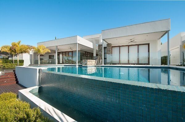 Modern white house with a large turquoise infinity pool under a clear blue sky