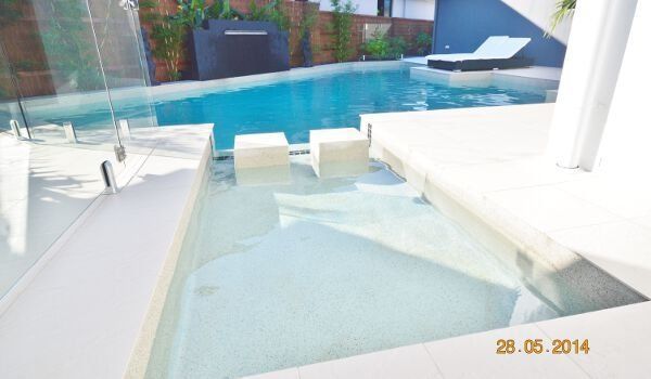 Modern poolside patio with white loungers and a small wading pool in front of a blue swimming pool