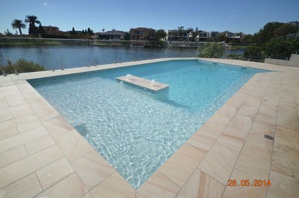 Modern backyard pool with clear blue water beside a lake under a sunny sky