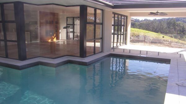 Modern house with a pool beside a patio, overlooking a sunny hillside landscape