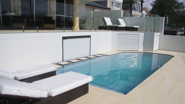 Modern rooftop pool with white lounge chairs and blue water beside glass walls
