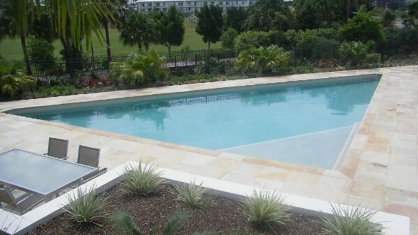 Outdoor swimming pool with blue water, surrounded by stone deck and landscaped greenery.
