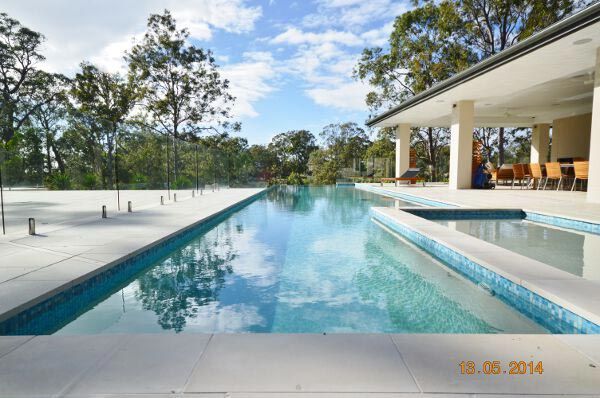 Modern outdoor pool beside a white patio and trees under a blue sky
