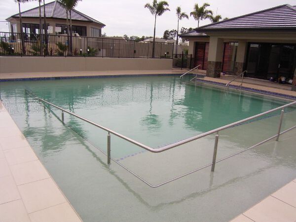 Outdoor swimming pool with a safety railing, surrounded by a tiled deck and resort buildings.
