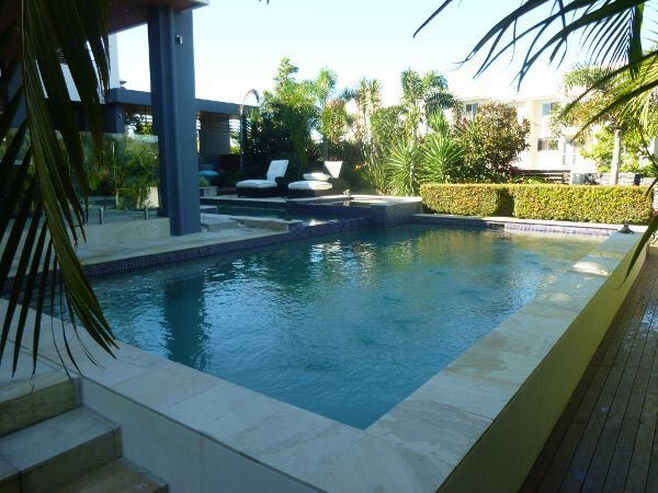 Modern backyard swimming pool with clear blue water, palm fronds, and a shaded patio area