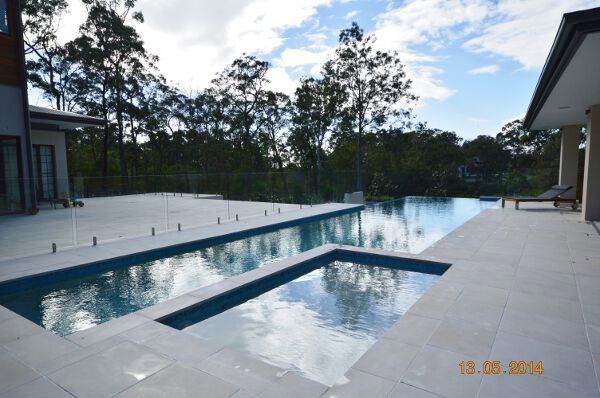 Modern backyard pool with blue water, white deck, and trees in the background
