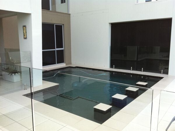 Modern courtyard with a shallow black-tiled reflecting pool and stepping stones beside white walls